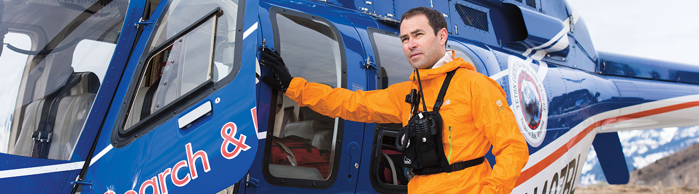 A man stands at the door to a helicopter in a mountainous area.